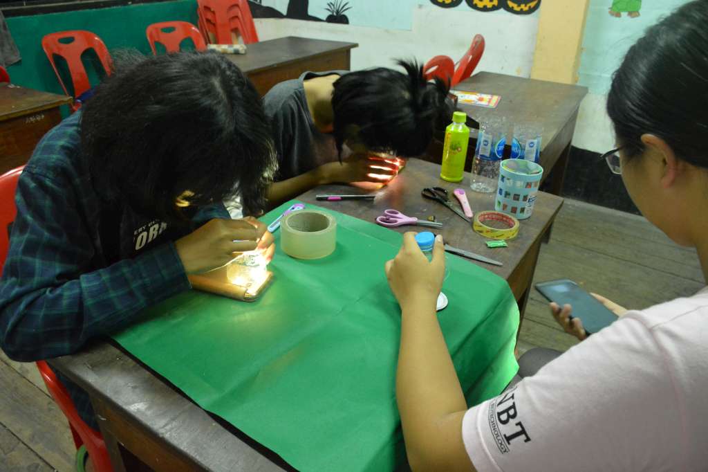 林俊宏每年帶領志工學生前往泰北協助科普教學，圖為協助當地學生製作簡易顯微鏡。