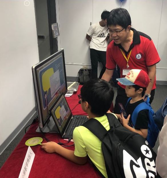 中研院院區開放工作人員帶著小朋友與小學數學解題機器人互動。
